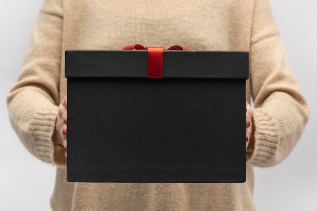 Gran caja de regalo negra con lazo rojo en manos femeninas Celebración