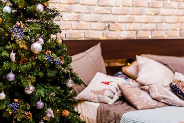 Una gran cama doble y un árbol de Navidad se apoyan contra una pared de ladrillos. Interior de año nuevo. Foto