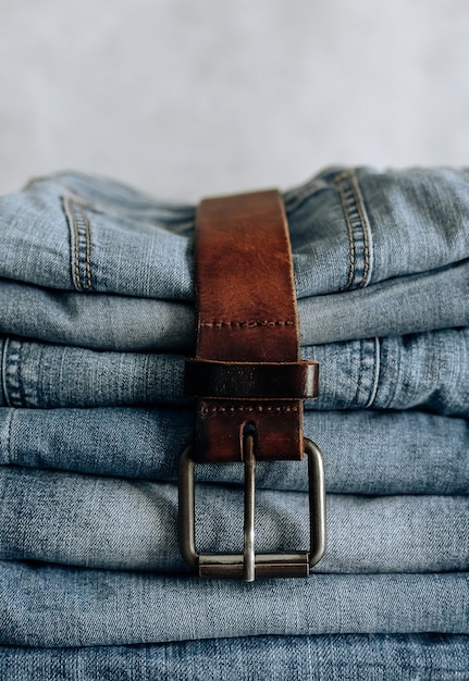 Foto gran cantidad de diferentes blue jeans blue jeans, pila de jeans y cinturón marrón.