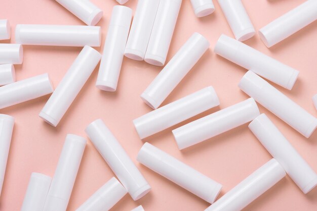Gran cantidad de tubos de brillo de labios de plástico blanco sobre fondo rosa