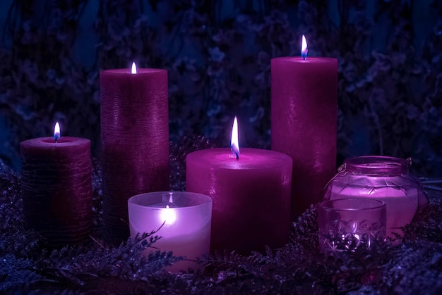 Una gran cantidad de velas mágicas de colores violeta púrpura y terciopelo arden en el fondo azul con flores.