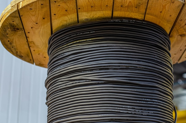 Gran carrete de madera con cable negro en el primer plano de la planta