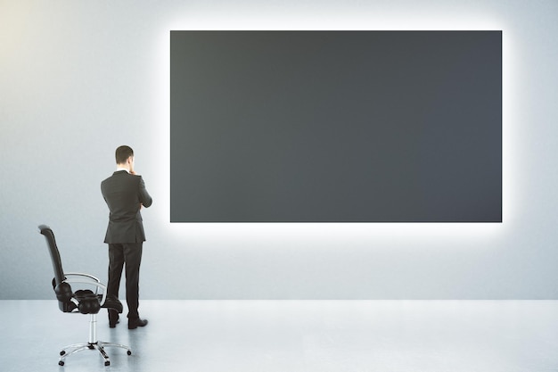 Un gran cartel en blanco y negro en la pared y un hombre de negocios con una imitación de una silla de cuero.