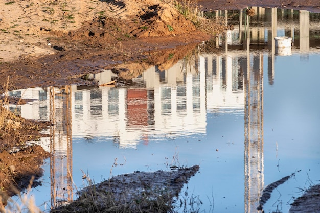 Un gran charco después de la lluvia en el sitio de construcción de un gran edificio residencial. Reflexión en el agua de un sitio de construcción y grúas en un día soleado.