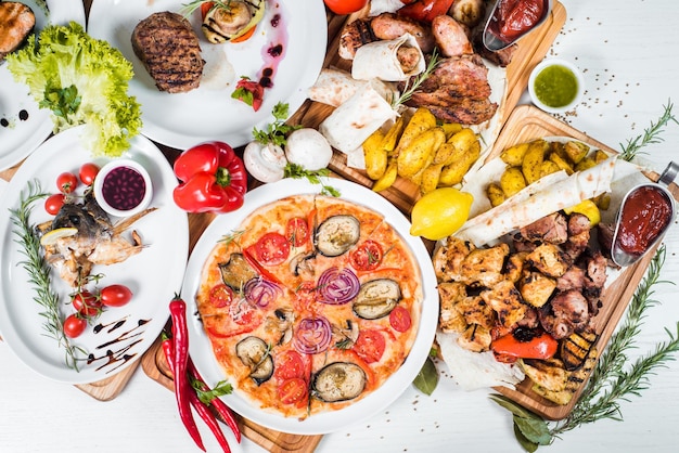 Gran conjunto de diferentes platos con carne, verduras, pizza y especias flatlay sobre fondo blanco.