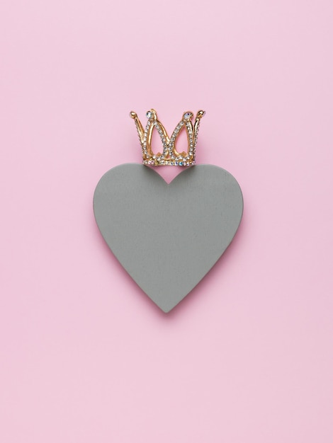 Foto un gran corazón gris y una corona sobre un fondo rosa claro. el concepto de amor y poder.