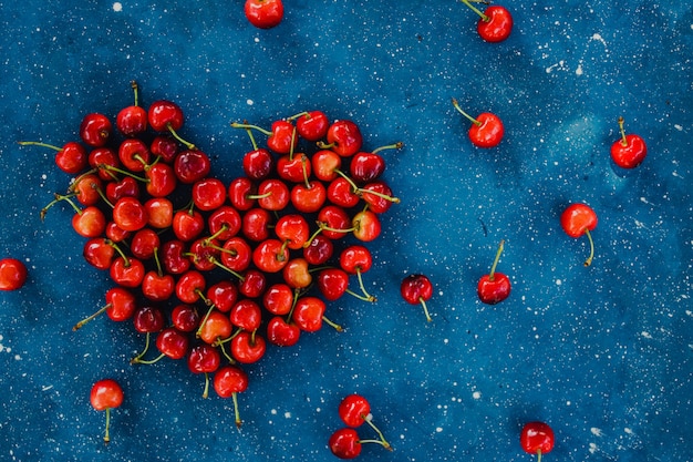 Foto gran corazón rojo hecho de cerezas maduras de cosecha propia en el fondo de hormigón azul