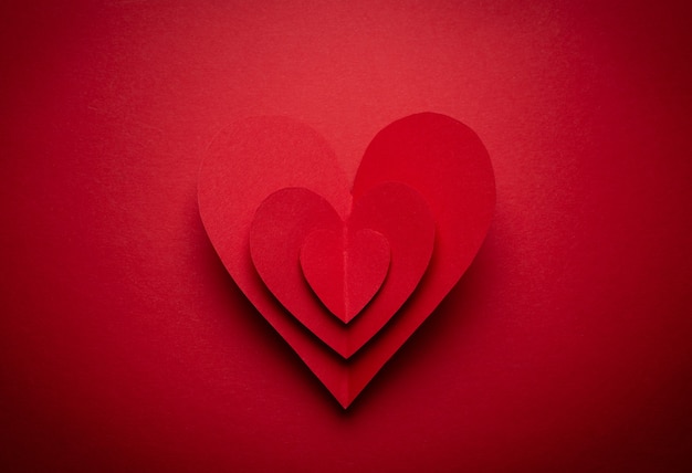 Gran corazón rojo voluminoso cortado de papel sobre fondo monocromático rojo, estilo origami artesanal de papel, desde arriba. Símbolo romántico del día de San Valentín, concepto de amor. Diseño de arte en papel, celebración del 14 de febrero