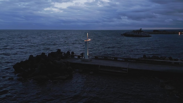 Una gran cruz cristiana se encuentra en el borde de un muelle contra un espectacular cielo y mar visto desde arriba