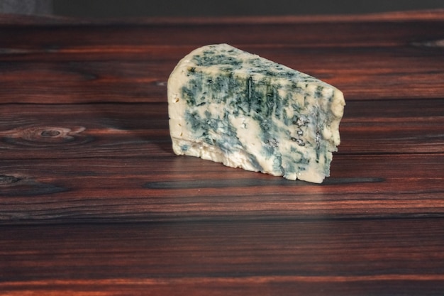 Gran cuña de queso azul sobre un fondo de madera oscura.