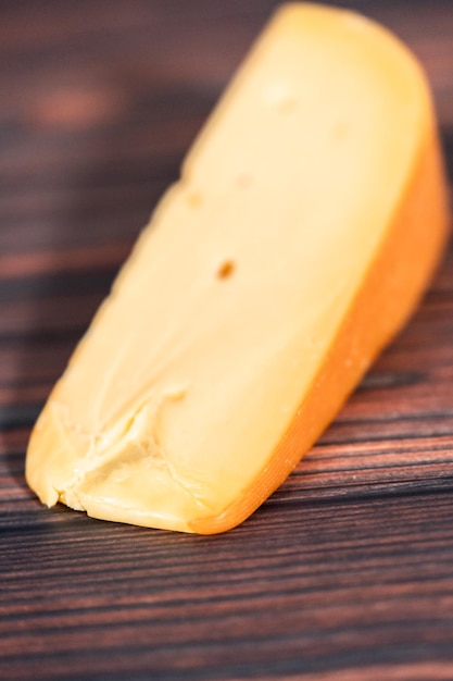 Gran cuña de queso Gouda ahumado sobre un fondo de madera oscura.