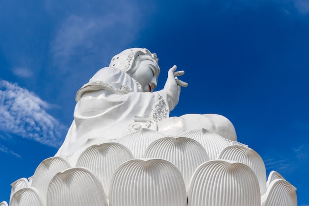 Una gran estatua blanca de Guan Yin detrás del cielo y la luz del sol durante el día.