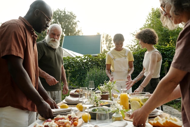 Gran familia intercultural feliz sirviendo mesa con comida y bebidas caseras