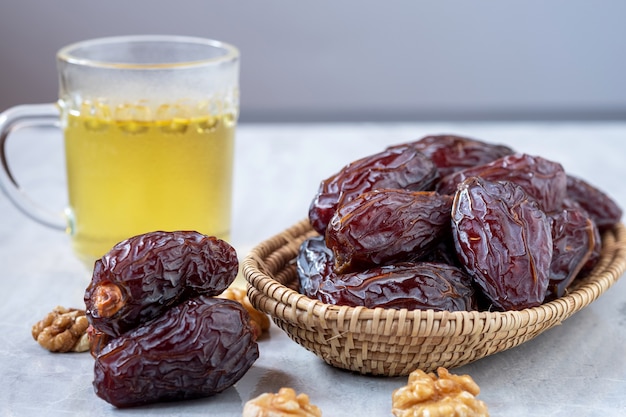 Foto la gran fecha de frutas medjool en canasta con nuez y té sobre un piso de mármol