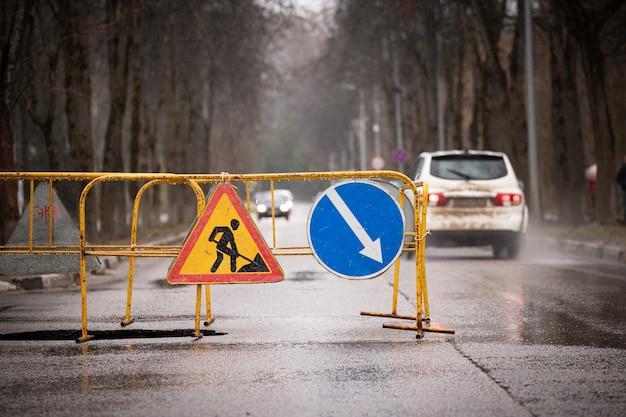 Gran foso en la carretera después de fuertes lluvias y hundimientos con una valla y señales de advertencia