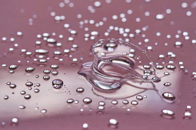 Foto una gran gota y salpicaduras de agua micelar en un fondo rosado