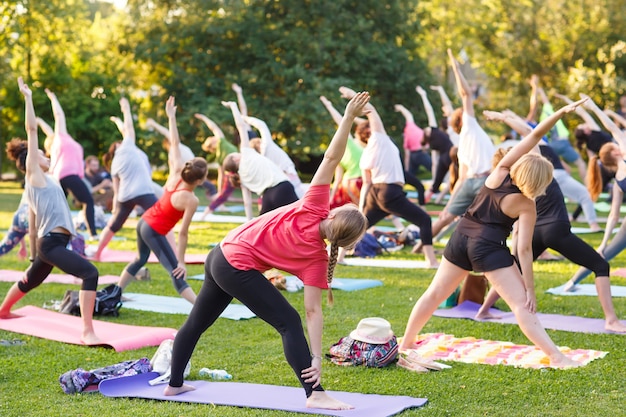 Gran grupo de adultos que asisten a una clase de yoga afuera en el parque