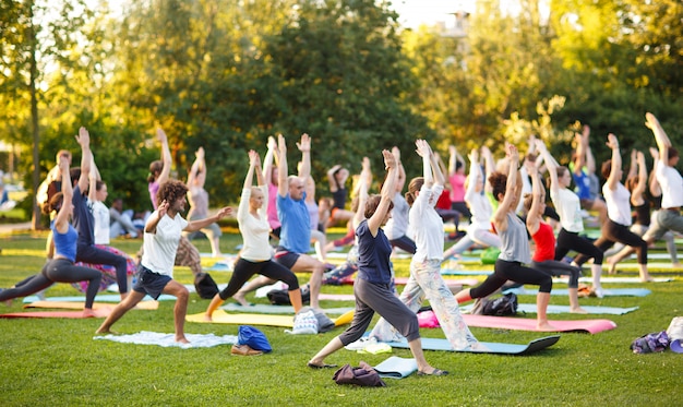 Gran grupo de adultos que asisten a una clase de yoga afuera en el parque