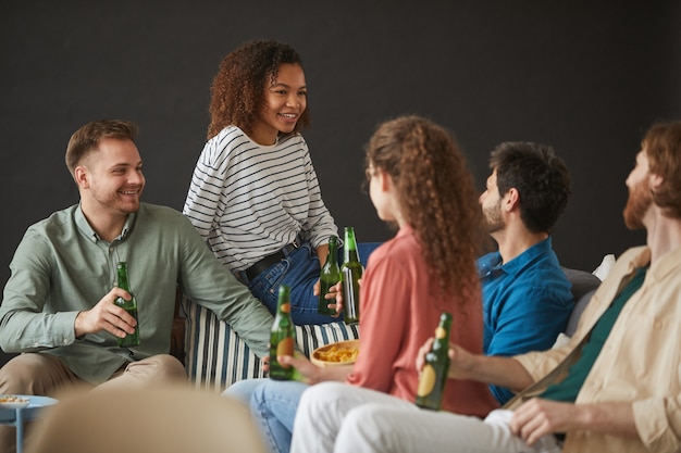 Gran grupo de amigos disfrutando de cerveza y bocadillos durante la fiesta en casa