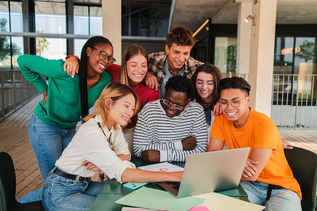 Gran grupo de estudiantes adolescentes reales buscando información juntos usando una computadora portátil en la universidad