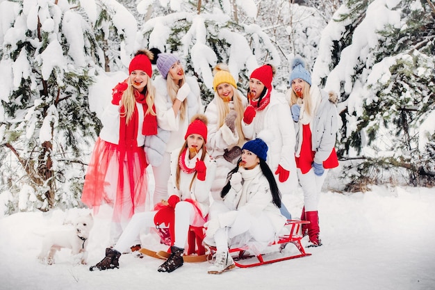 Un gran grupo de niñas con piruletas en sus manos se encuentra en el bosque de invierno. Chicas en ropa roja y blanca con dulces en un bosque cubierto de nieve.