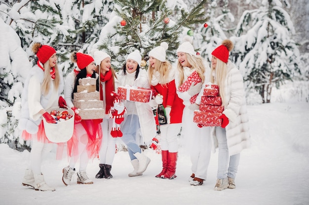 Un gran grupo de niñas con regalos de Navidad en sus manos de pie en el bosque de invierno.Niñas en ropa roja y blanca con regalos de Navidad en el bosque nevado