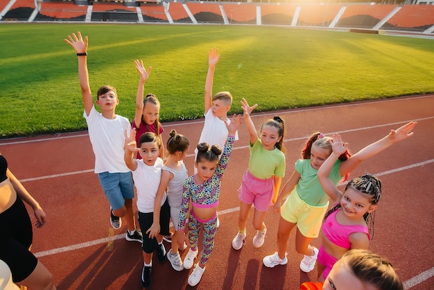 Un gran grupo de niños y niñas se paran juntos en un círculo y se doblan las manos afinando y elevando el espíritu de equipo antes del partido en el estadio durante la puesta de sol Un estilo de vida saludable