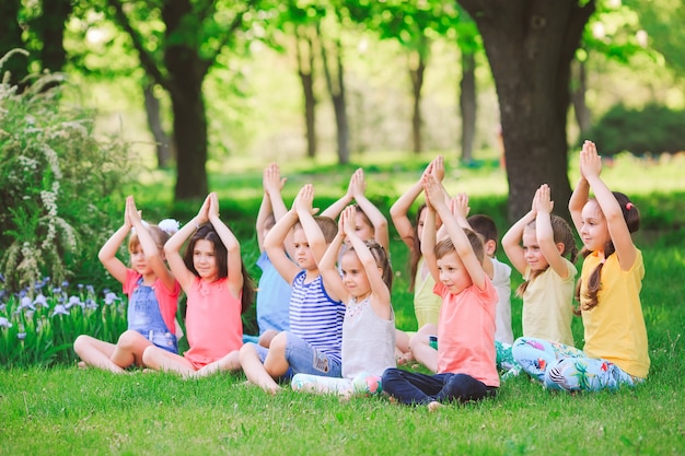 Un gran grupo de niños practicando yoga en el parque sentados en el césped.