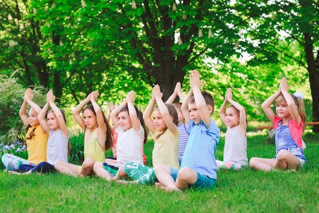 Un gran grupo de niños practicando yoga en el parque sentados en el césped.