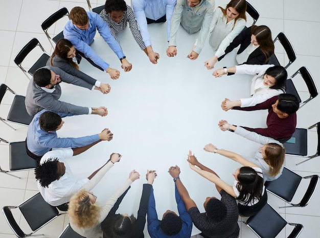 Un gran grupo de personas sentadas en una mesa redonda con los brazos extendidos