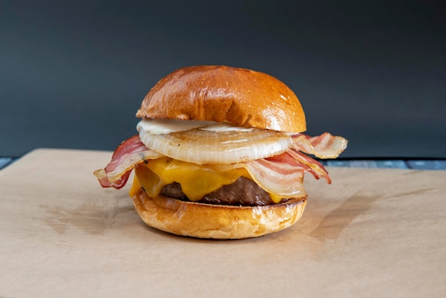 Gran hamburguesa clásica cocinada a la parrilla con mucho tocino frito rebanadas de cebolla blanca crujiente queso cheddar derretido mayonesa y carne de res