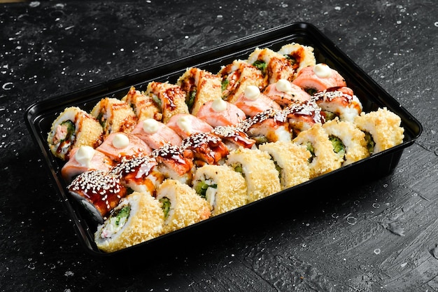 Gran juego de rollos de sushi con queso y pescado y caviar comida japonesa entrega cubiertos desechables sobre un fondo de piedra negra