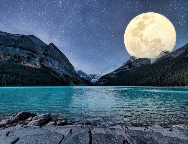 Foto gran luna brillando sobre montañas rocosas y estrellada en lake louise en la noche en el parque nacional banff