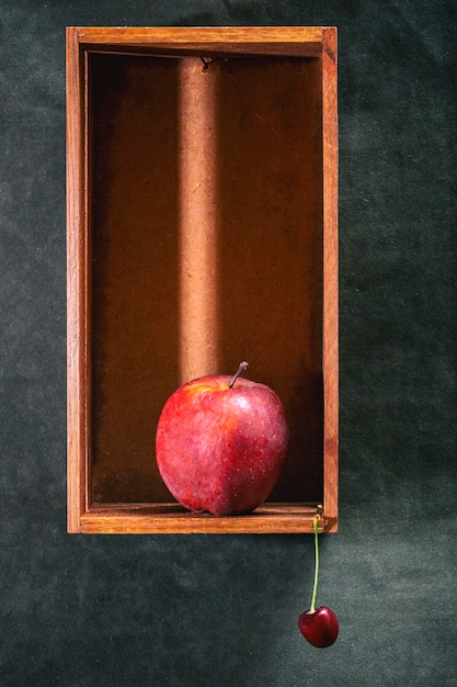 Foto una gran manzana roja en una caja de madera y cerezas maduras