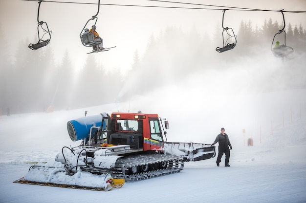 Gran máquina de limpieza de nieve trabajando en la pista de esquí bajo sillas de cable