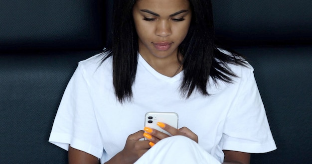 Gran mensaje de la mañana. Hermosa joven africana acostada en la cama y usando su teléfono inteligente.