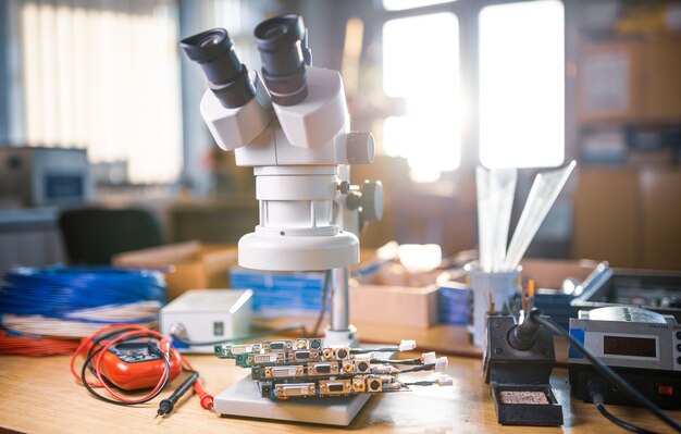 Un gran microscopio electrónico moderno y microcircuitos integrados se apilan en la placa de prueba para prepararse para la investigación de componentes electrónicos en un laboratorio científico.