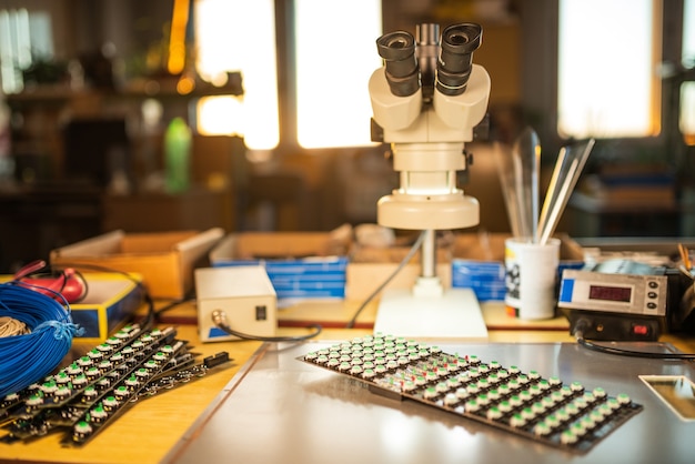 Un gran microscopio electrónico y un panel de indicadores de luz LED se apilan en una placa para preparar la investigación de componentes electrónicos en un laboratorio.