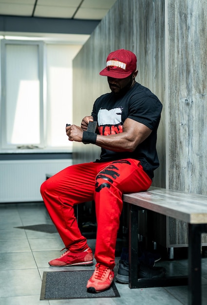 Gran modelo de fitness de hombre fuerte descansando en el gimnasio. se apoyó contra el equipo deportivo del simulador. Gorra negra y camiseta, descanso.