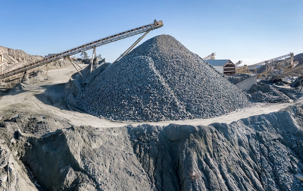 Gran montón de grava y maquinaria en la planta de trituración y cribado de piedra, sobre el cielo azul