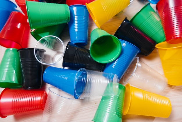 Un gran montón de vasos de plástico multicolores esparcidos por el suelo. Contaminación del medio ambiente por desechos humanos.