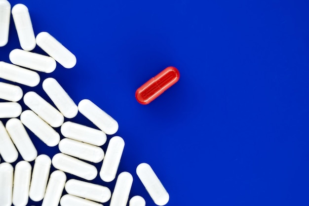 Gran número de pastillas blancas esparcidas en una superficie azul entre las pastillas blancas una sola pastilla roja