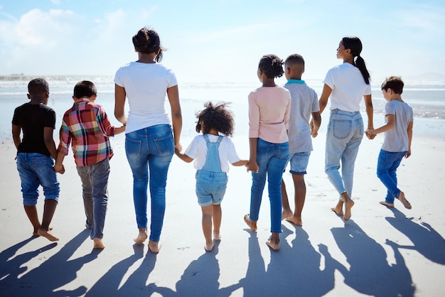 Gran paseo familiar por la playa y verano para disfrutar del sol de vacaciones y vincularse con la diversidad interracial junto al agua Familia feliz madre lesbiana y tomados de la mano para el cuidado solidario y el amor en vacaciones junto al mar