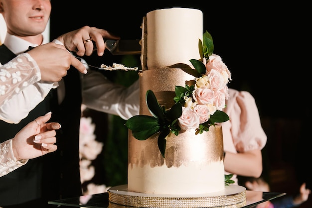 Gran pastel de bodas blanco de varios niveles con flores retroiluminadas recién casados cortan el pastel