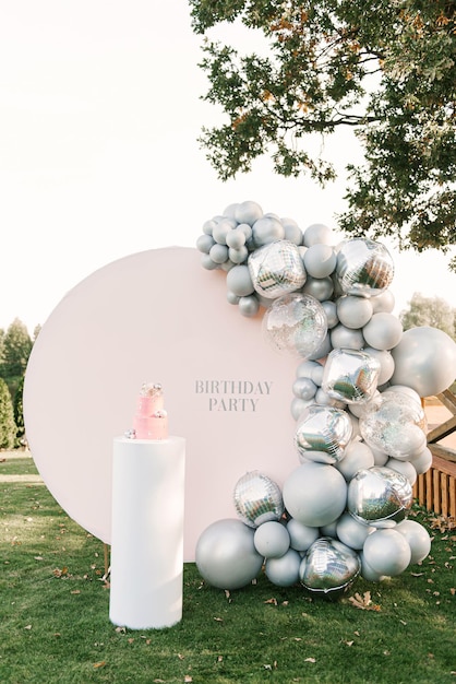 Un gran pastel rosa con una zona de fotos rosa de globos plateados en el fondo Fiesta decorada con globos