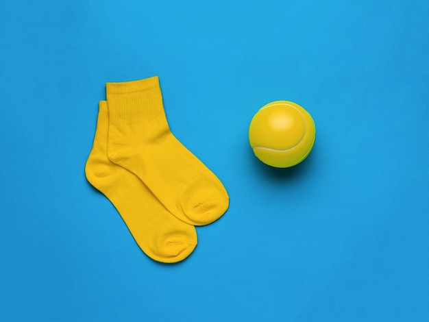 Una gran pelota de tenis amarilla y calcetines amarillos sobre un fondo azul El concepto de deportes femeninos Plano