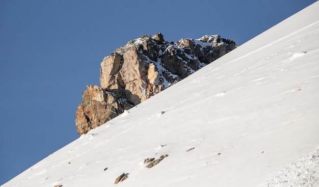 Una gran piedra en la ladera nevada de la montaña y el cielo azul