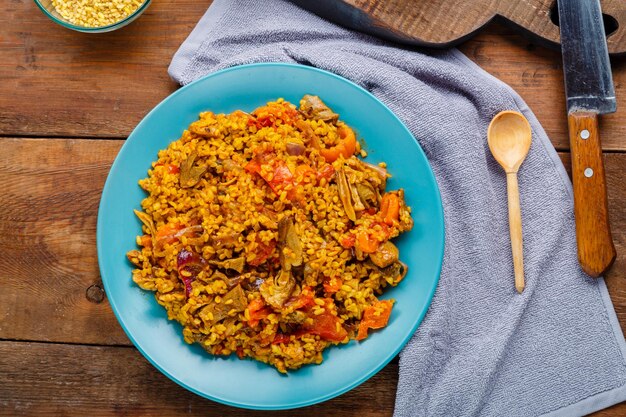 Un gran plato de bulgur con verduras y champiñones sobre una mesa en una servilleta junto a una cuchara de madera