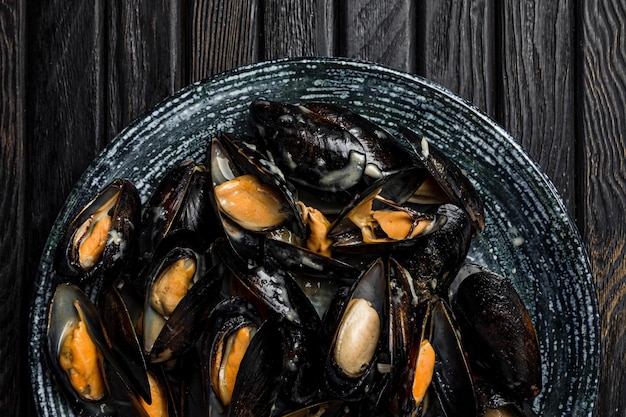 Un gran plato de mejillones con salsa de pan blanco a la parrilla y una rodaja de limón tomada desde arriba de un fondo de madera oscura cerrado