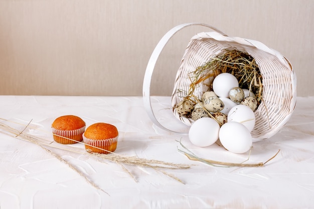 Gran pollo blanco y huevos de codorniz en una canasta con paja sobre una mesa de madera de luz blanca